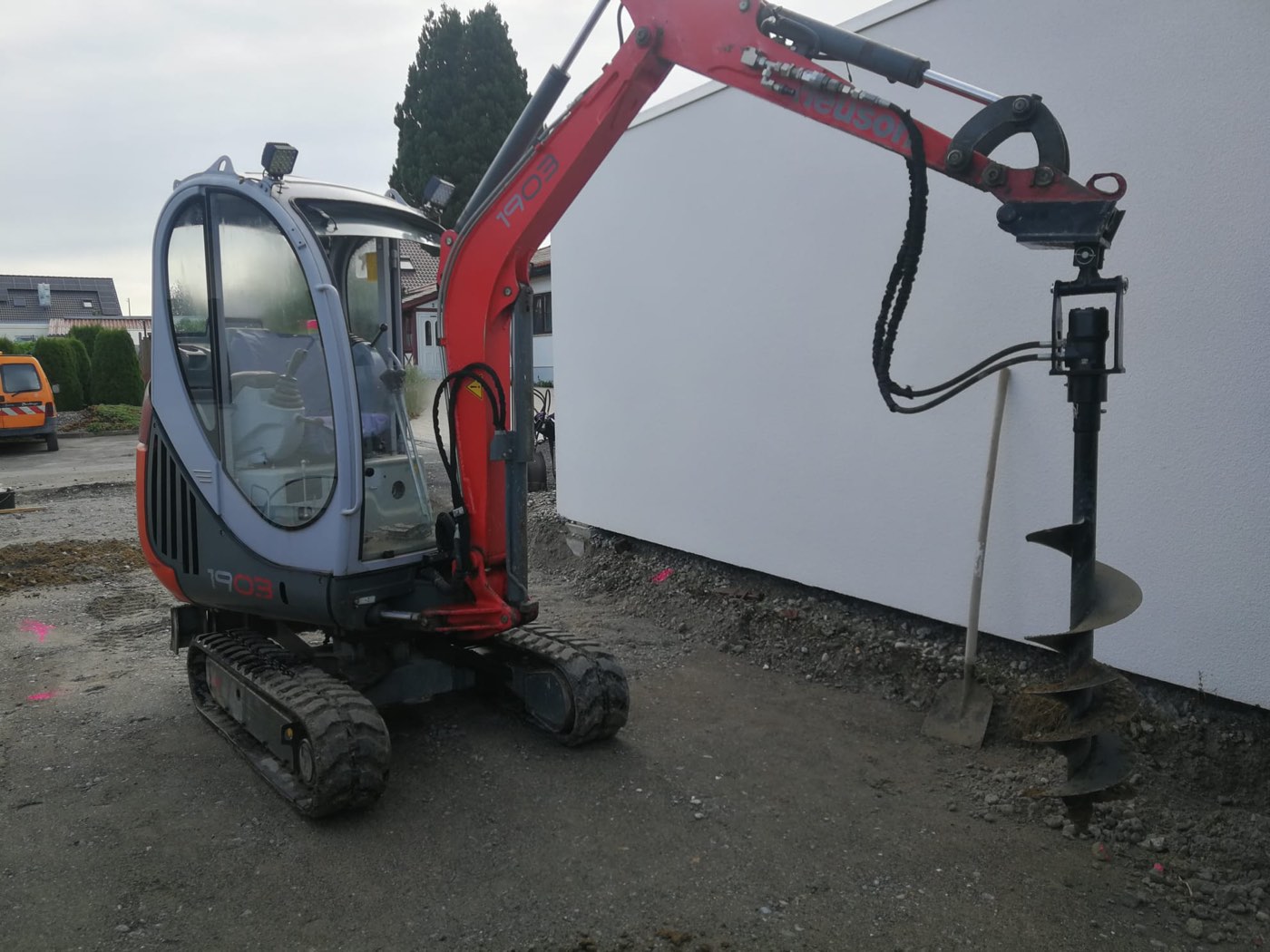 Minibagger Neuson 1903 mit Erdbohrer an einer Hauswand