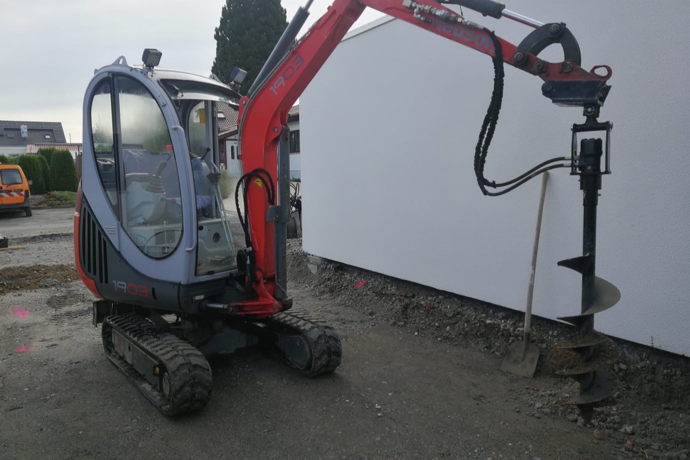 Minibagger Neuson 1903 mit angebautem Erdbohrer auf einer Baustelle neben einem Hausneubau